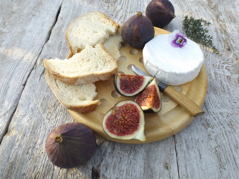 Cheeseboard. Brie cheese, bread and figs on a round wooden board.