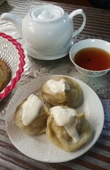 Uzbek national dish of manti, khinkali, pelmeni, Pirogi, or dumplings with liver served with sour cream and bread sprinkled with sesame seeds. on the table is a kettle with green tea with