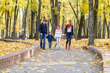 A happy family having fun in the park in autumn walking and hugging. Family, love, happiness concept. Family of four with mother father sister and a little cute brother