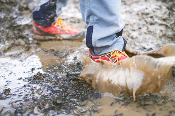 Detail of trekking boots in a mud. Muddy hiking boots and splash of water. Man splashing in muddy and water in the countryside.