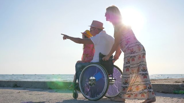 parents with child on rest happy pregnant woman with little girl and handicapped person in backlight daughter sits on disabled daddy in wheelchair