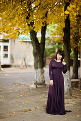 Adult brunette woman at violet gown on autumn fall background.