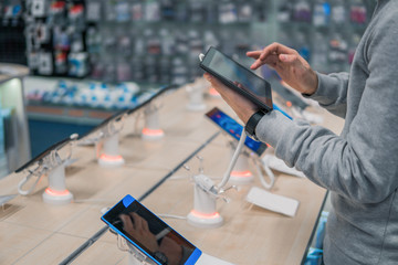 Closeup view of male customer hands, choosing digital tablet in the mobile phone shop. difficult decision. Various choice