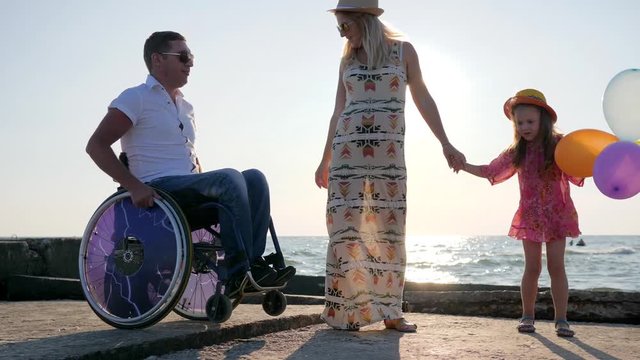 disabled man in wheelchair with daughter and wife on background blue sky family having fun at summer holidays