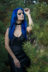 Beautiful woman with dark blue hair dressed in black dress in the magic forest
