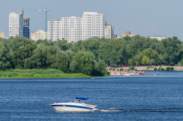 Fototapeta na wymiar Boat sails along the Dnipro River in the background of the buildings of Kiev
