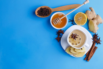 Hot spicy ginger tea in white cup with lemon, honey and spices on blue background, flat lay with copy space
