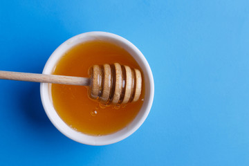 Honey with wooden honey dipper on blue background, view from above