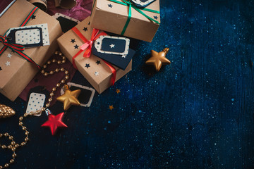 Decorations and wrapped presents concept. Christmas celebration dark flat lay with craft paper boxes, stars, tags, garlands and copy space on a dark wooden background.
