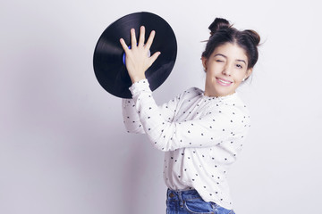 Girl holding a vinyl record, playing with it, indoors, over a white wall.