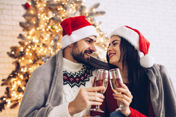 Christmas hugging couple cheers together near ornate festive Eve on Sata Claus hats. Holidays celebrations family  together