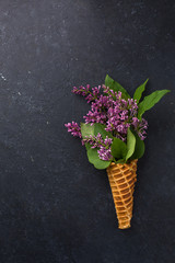 Ice cream cone with lilac branches on a black concrete background. Fresh flowers. beautiful bouquet of flowers. Copy Space. View blank space for text. Place for text. Food photo. Flat lay, top view