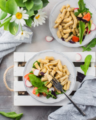 Homemade gnocchi. A traditional Italian dish. Gnocchi with oil of spices and a salad of fresh vegetables and herbs: radish, tomato, arugula, basil. On a light concrete background  Flat lay, top view