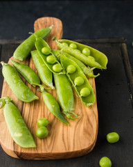 Young green peas on an olive wood board on a concrete black background Place for text. Flat lay, top view