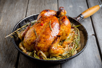 Roasted chicken in pan on the rustic wooden background. Selective focus.