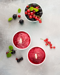 Frozen berry smoothies in bright paper cups on a light gray concrete background with fresh red currant and black gooseberry. place for text. flat lay, top view