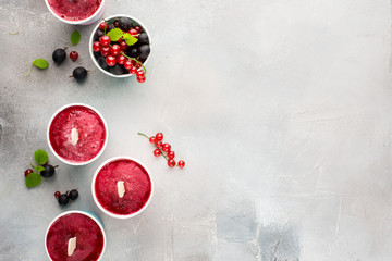 Frozen berry smoothies in bright paper cups on a light gray concrete background with fresh red currant and black gooseberry. place for text. flat lay, top view