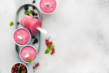 Frozen berry smoothies in bright paper cups on a light gray concrete background with fresh red currant and black gooseberry. place for text. flat lay, top view