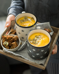 Pumpkin soup with coconut milk, pumpkin seeds and spices in vintage blue mugs on a gray concrete background. Atmospheric dark food photo. 
