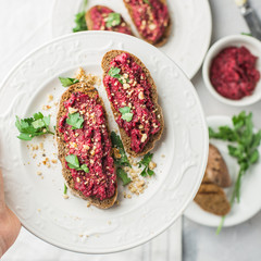 Homemade toast from whole grain bread with beet paste, greens and nuts. Light concrete background, white soft. Place for text. Food photo with hands. Useful dietary baking. Flat lay, top view