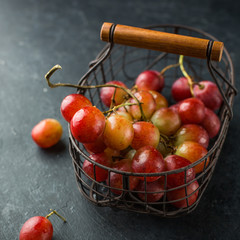 Red large grapes on a branch in a vintage iron basket on a concrete black background. Fresh fruits, beautiful card or background