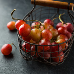 Red large grapes on a branch in a vintage iron basket on a concrete black background. Fresh fruits, beautiful card or background