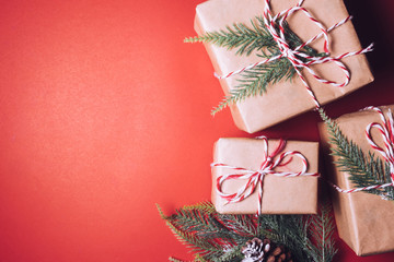 Top view of gift packages wrapped in brown paper with fir tree branch on red background. Free space for text
