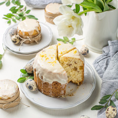 Traditional Easter cake on a light wooden background. Decorated with flowers. Next to a small cake, quail eggs and flowers. Cut a piece of cake. Easter. Celebration. Spring. Rustic style