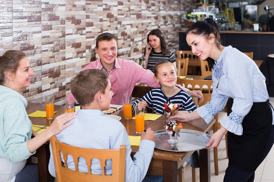 vigorous brunette waitress serving cheerful family in comfy family cafe