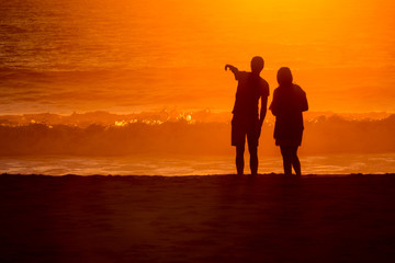 silhouetted couple loverlooking sunset washed waves