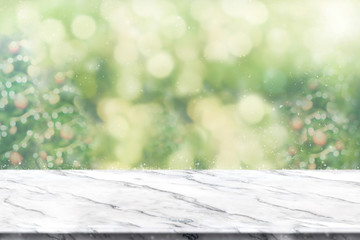 Empty white marble table top with abstract green blur christmas tree and snow fall background with...