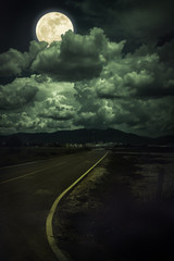 Dark sky with full moon and roadway through suburban zone.