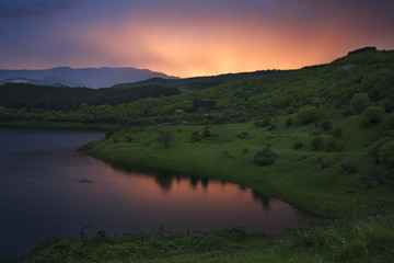 Beautiful view of the lake, green mountains, forest and bright sunset