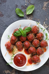 Wooden skewers with baked meatballs and sauce on a white plate, view from above, vertical shot