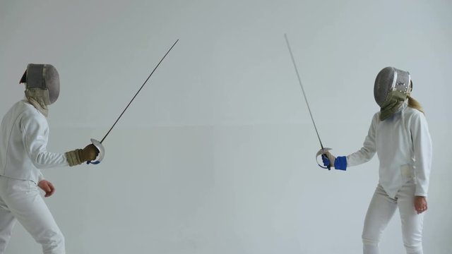 Two fencers have fencing match on white background indoors