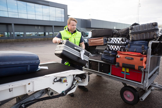 Worker Stacking Luggage On Trailer From Conveyor On Runway