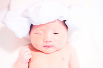 Newborn baby with hat sleeping on bed