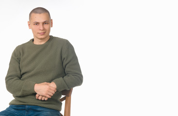 Fototapeta premium A young man is a skinhead in a green military style sweater. Studio. the guy sits on the boxes