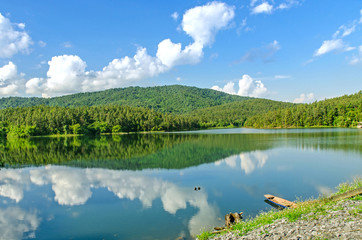 Landscape of the dam and lake on the mountain with tree and forest and the boat parked by the river with blue sky and clouds.