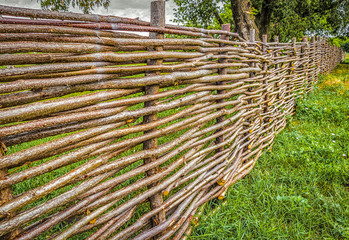 Rural wicker fence closeup on a green meadow.