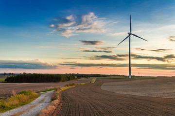 Obraz premium Amazing sunset at brown field with wind turbine in autumn