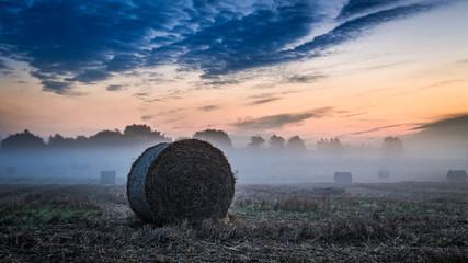 Dawn at foggy valley in autumn with hay on field