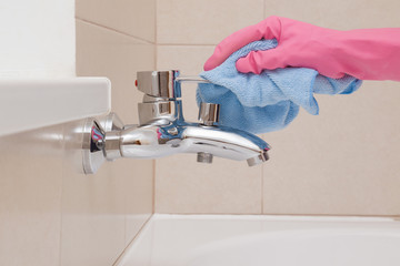 Employee hand in rubber protective glove with rag washing and polishing a water tap. Maid or housewife cares about house. Spring general or regular clean up. Commercial cleaning company concept.