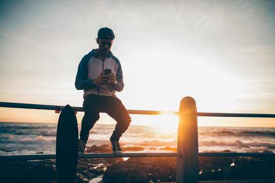 Hipster guy sitting on railing browsing with his smart phone