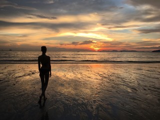 A woman on a beach in Thailand is looking at the sunset