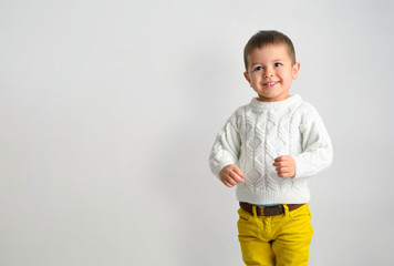 A happy smiling boy in a white sweater and yellow jeans are waiting for a gift.