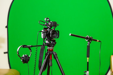 Video camera on a tripod, headphones and a directional microphone on a green background. The chroma...