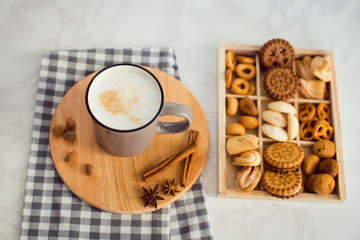 Cup of hot cappuccino with milk foam, cinnamon and different types of biscuits