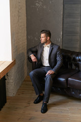 Man model in dark suit, white shirt on the dark couch
