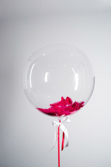 Large balloon with red feather inside hangs on white background